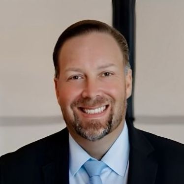 A man with a beard is wearing a suit and smiling.