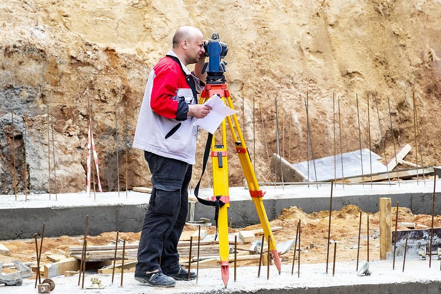 Surveyor using a theodolite on a construction site, taking measurements.