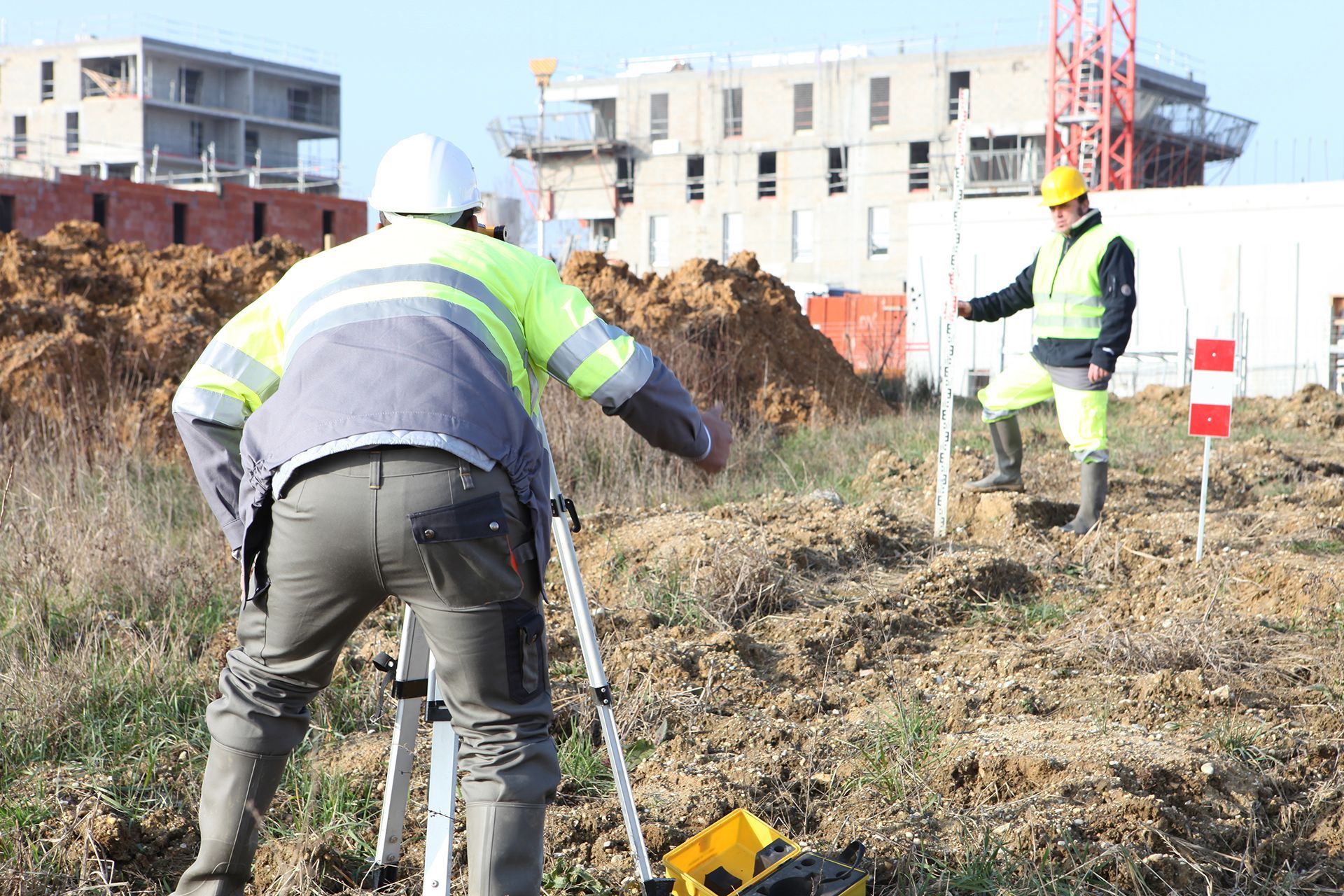 Two construction workers in safety vests surveying a construction site with equipment.