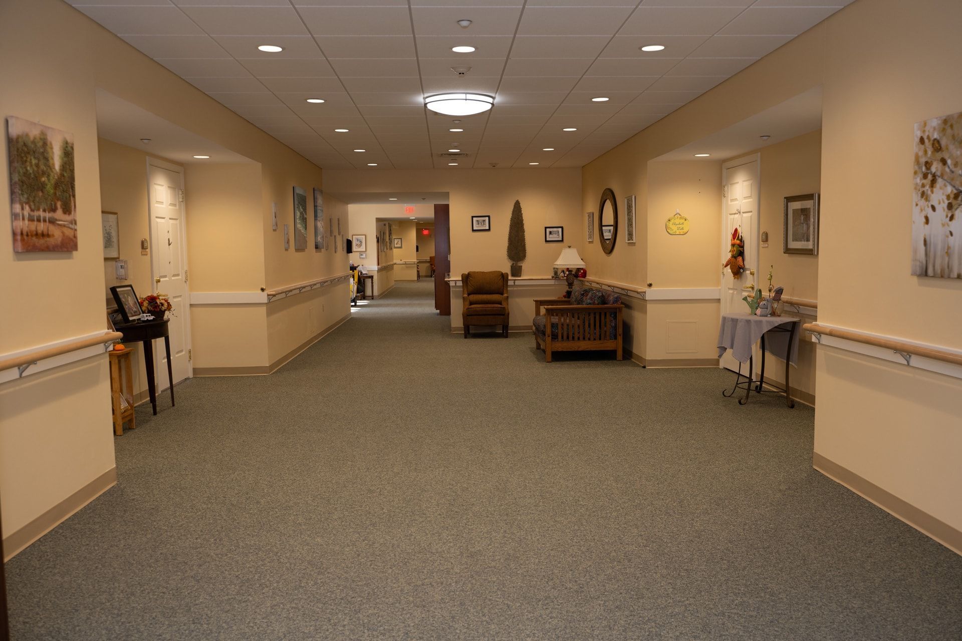Long hallway in a building with carpet, neutral-colored walls, artwork, handrails, and seating areas.