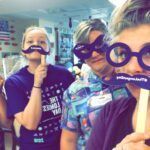 Three people with fake mustaches and glasses, posing in a brightly lit room.