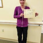 Woman in purple hoodie and black pants holding a sign that says 
