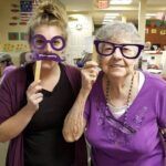 Two women smiling, holding purple glasses and mustache props