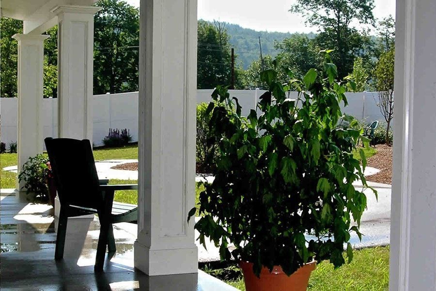 Porch with potted plant, chair, and view of yard with trees and mountain in the background.