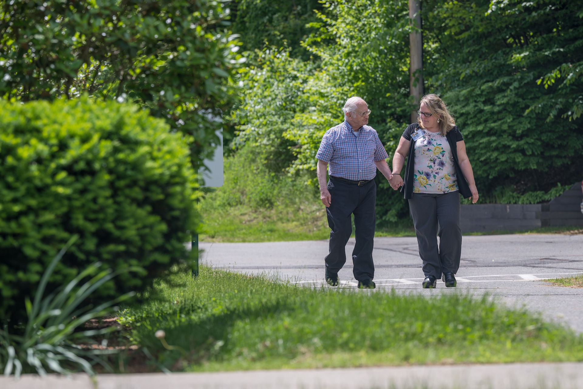 Man and woman walking on a path, holding hands; sunny outdoor setting.