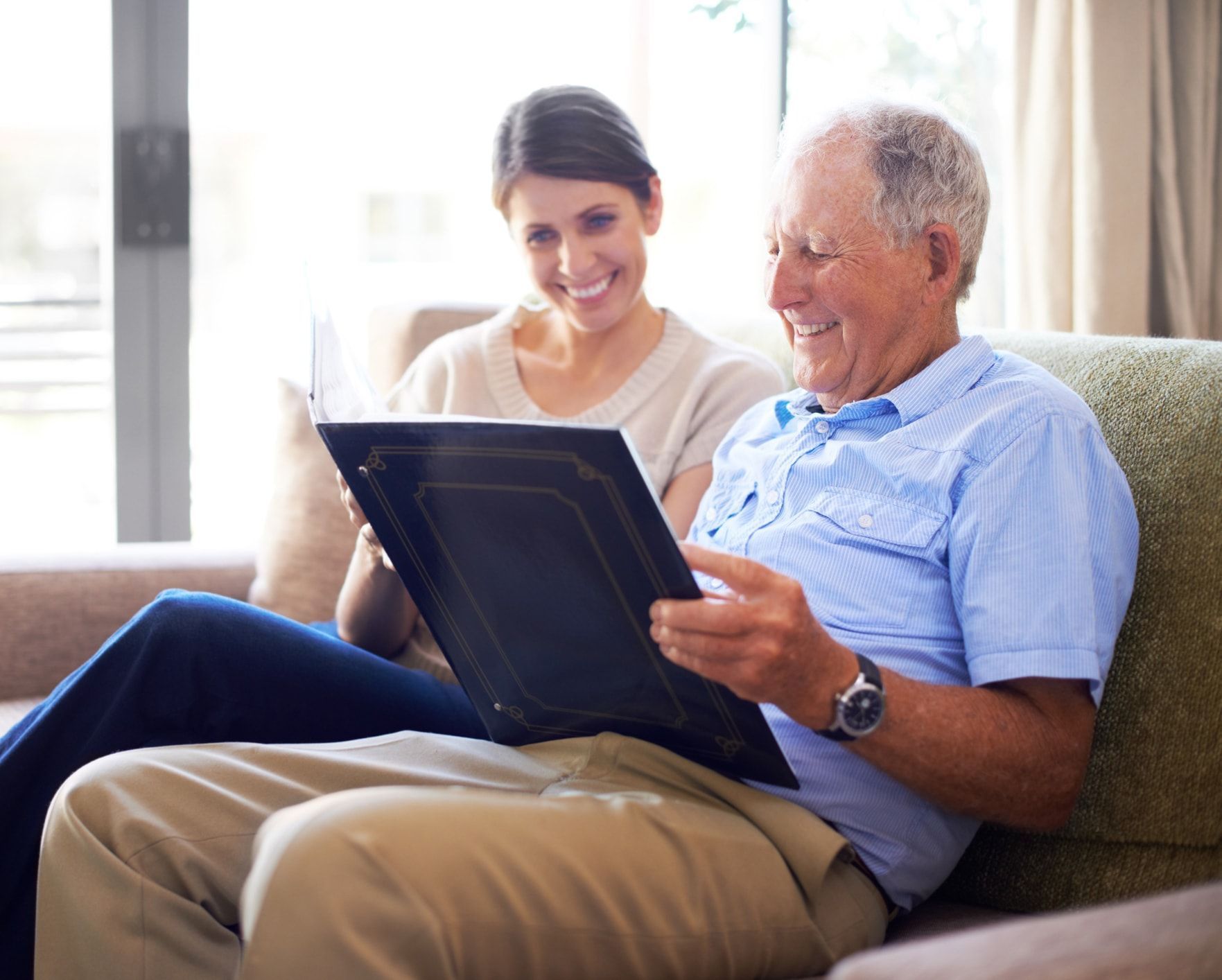 A smiling older man and woman looking at a photo album together on a couch.