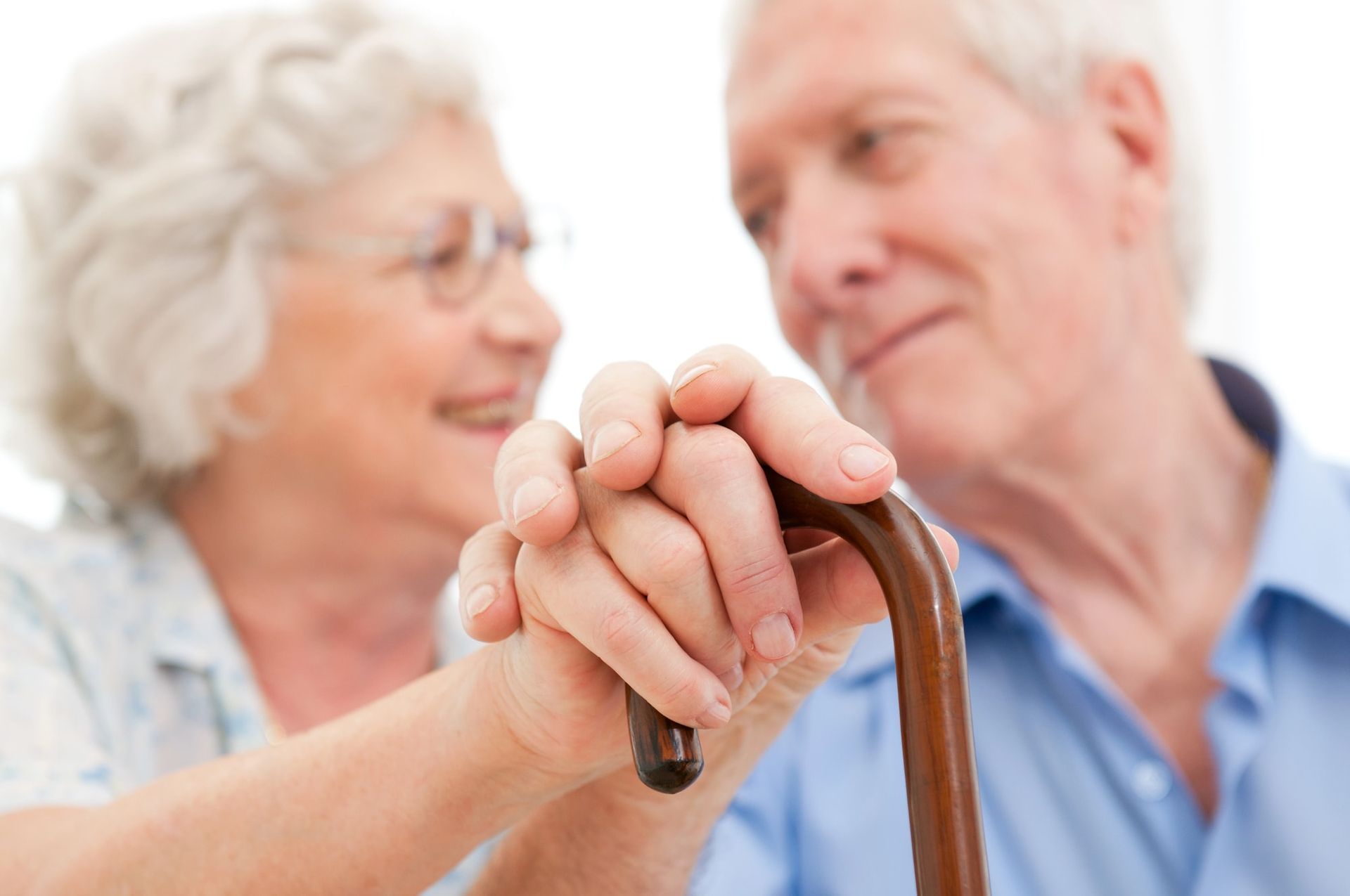 Elderly couple holding hands over a cane, smiling, soft focus.