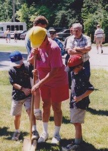 People planting, including a woman in pink and two boys, in a grassy area. Others observe in background.
