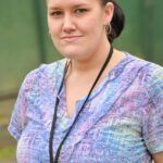 Woman in pastel scrubs with a black lanyard, looking at the camera with a slight smile.