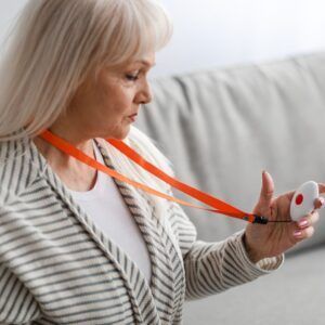 Woman holding medical alert pendant, wearing orange lanyard.
