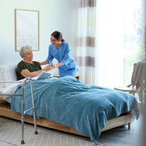 Nurse giving water to a person in bed, in a bedroom with a walker.