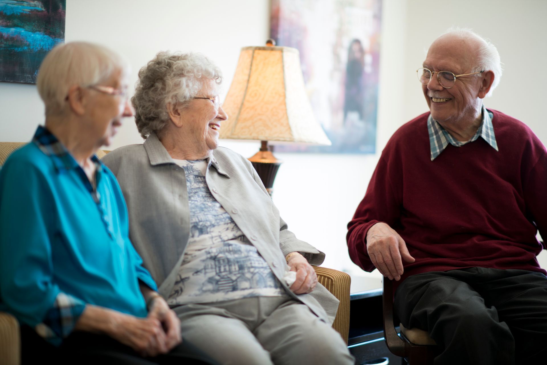 Three older adults sitting and smiling in a well-lit room, possibly a waiting area.