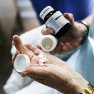 Hands holding prescription medication bottles and pills.