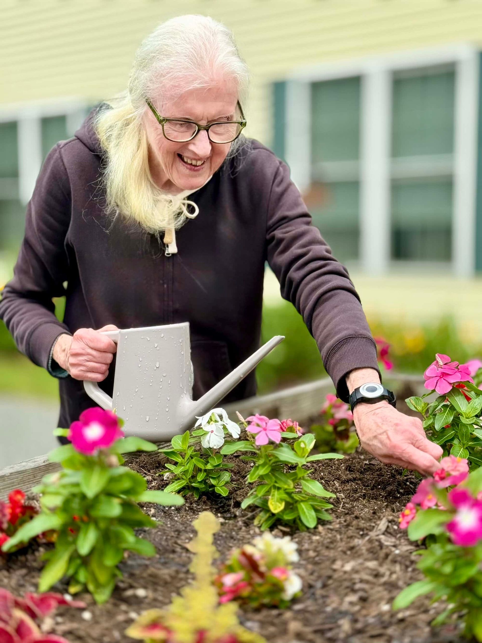 Woman smiling while watering flowers in a raised garden bed.