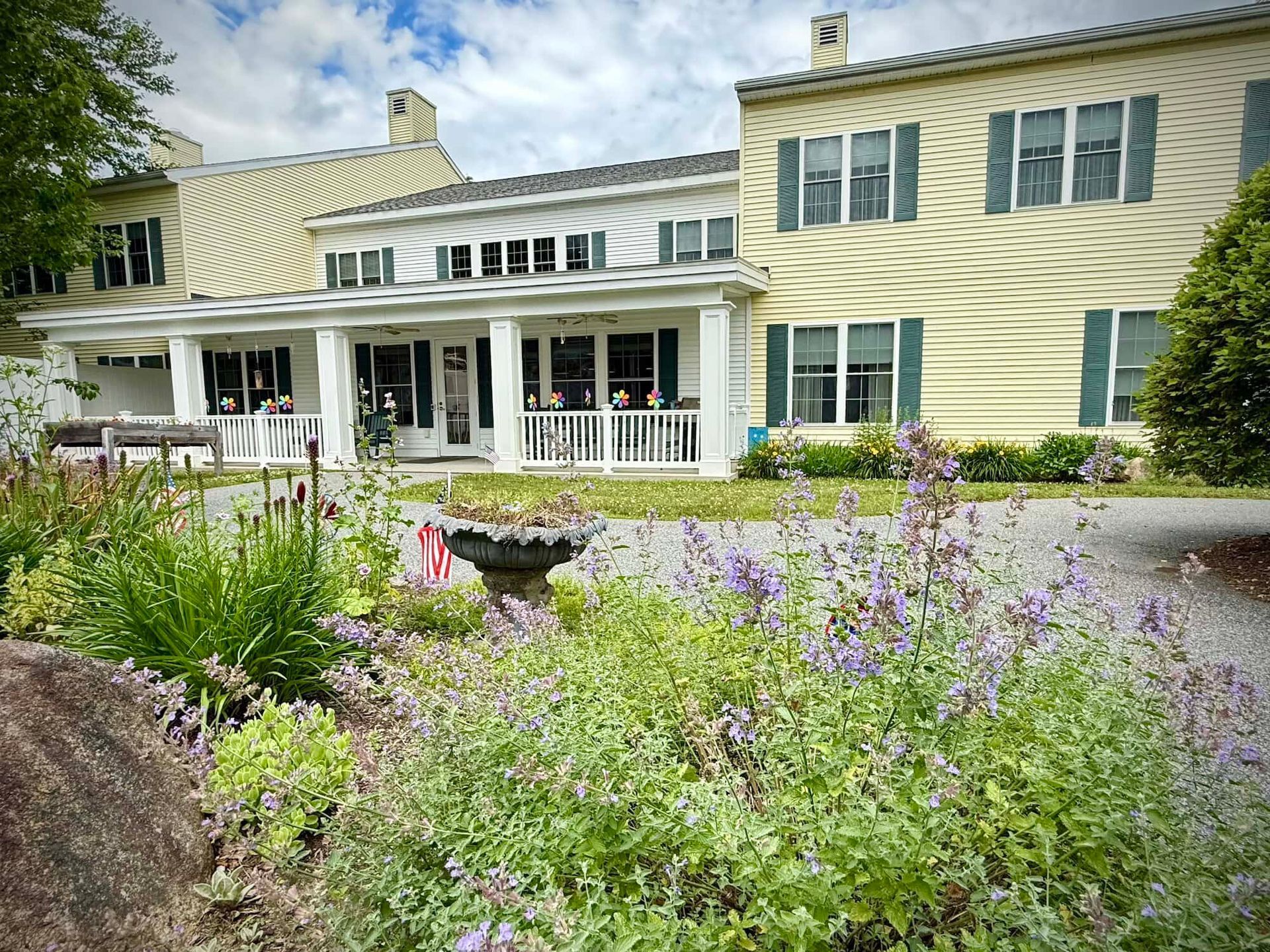 Yellow and white house with porch, garden in foreground.