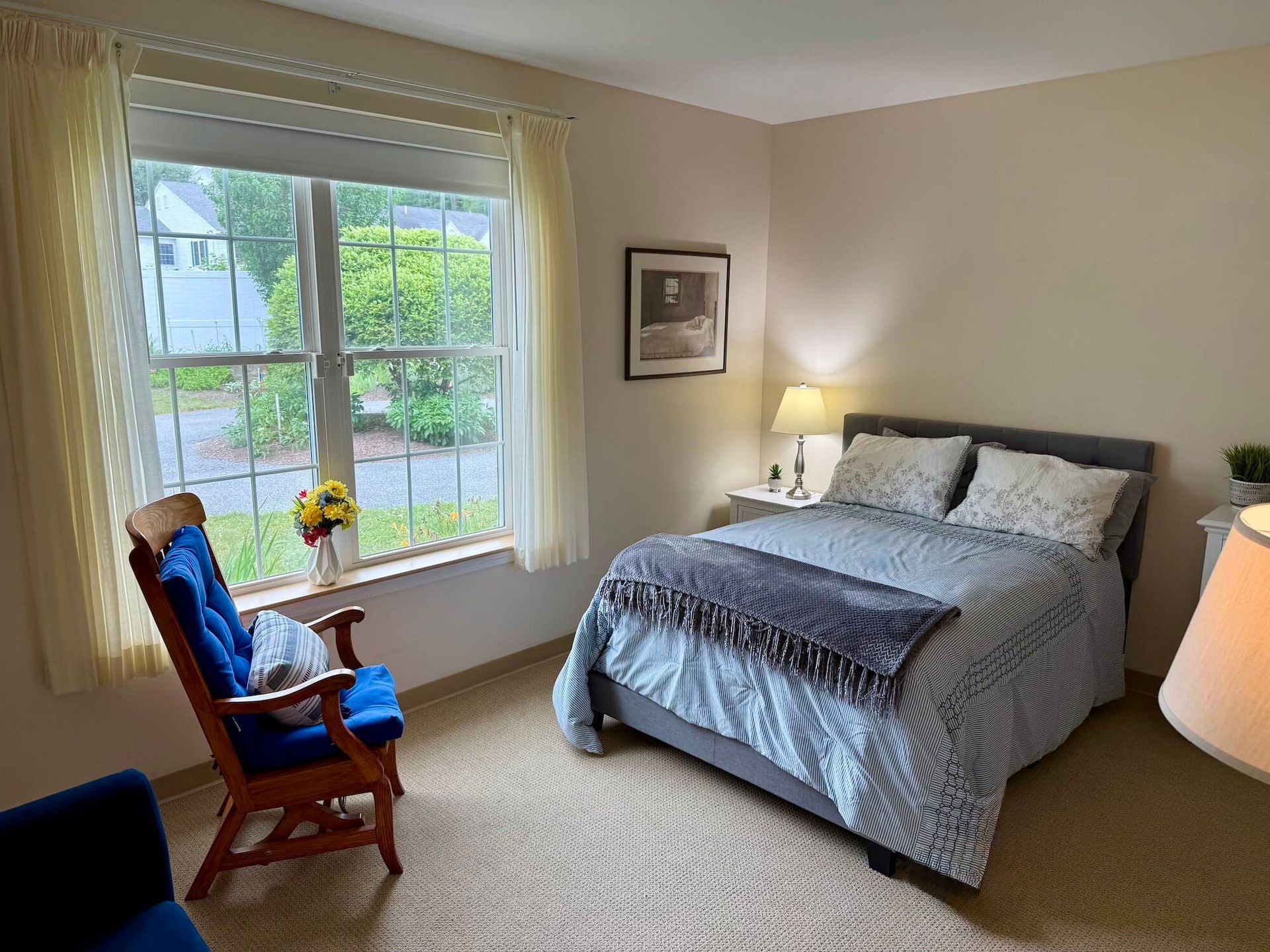 Bedroom with a bed, a window with curtains, and a blue rocking chair.