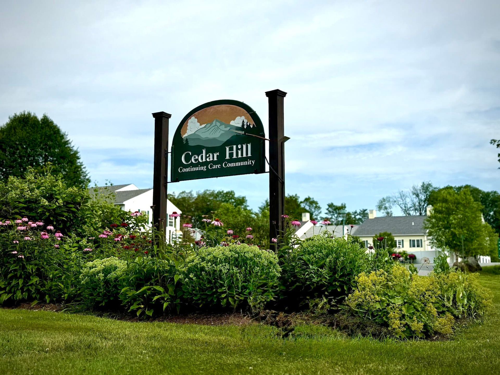 Sign for Cedar Hill with a landscape image; set in front of green shrubs and residential buildings.