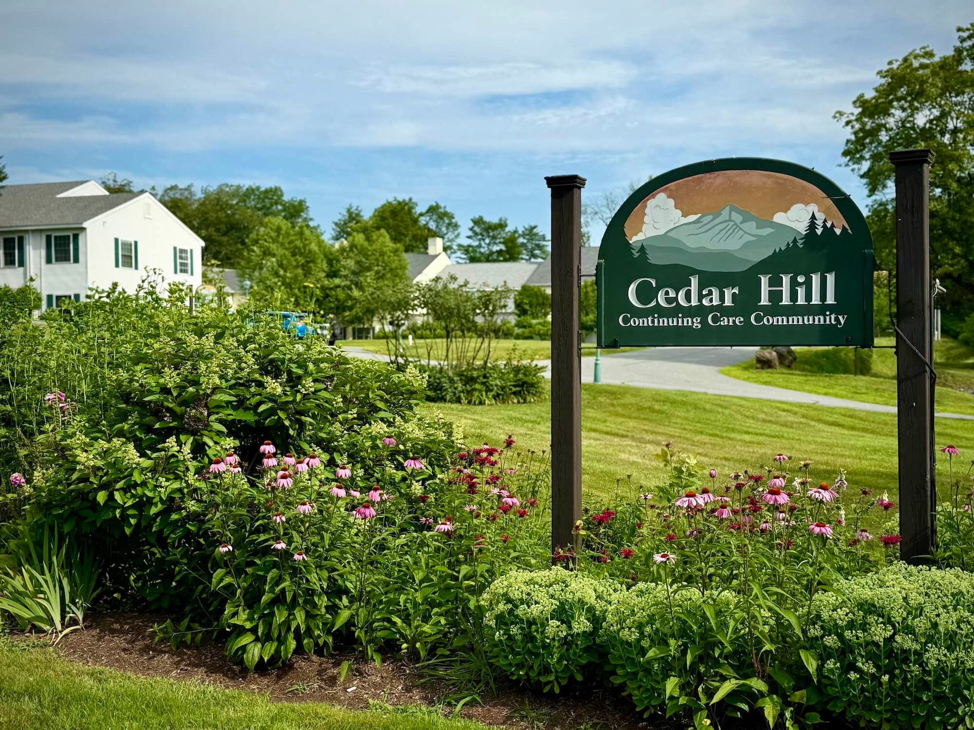 Yellow building with gray roof and green shutters, in a grassy area, with a parked car.