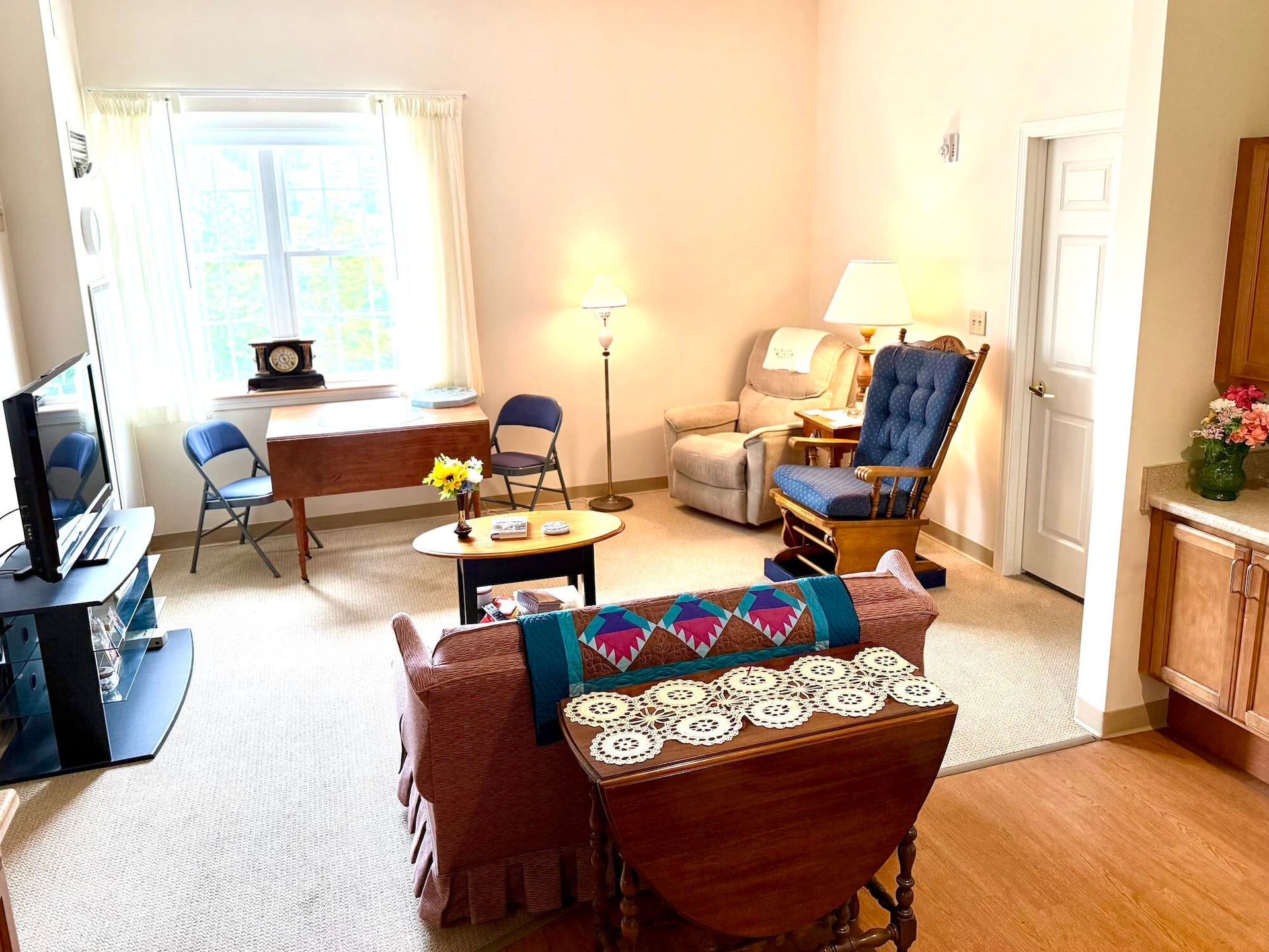 Living room with furniture, including sofa, chairs, table, and TV. Bright, neutral colors and natural light.