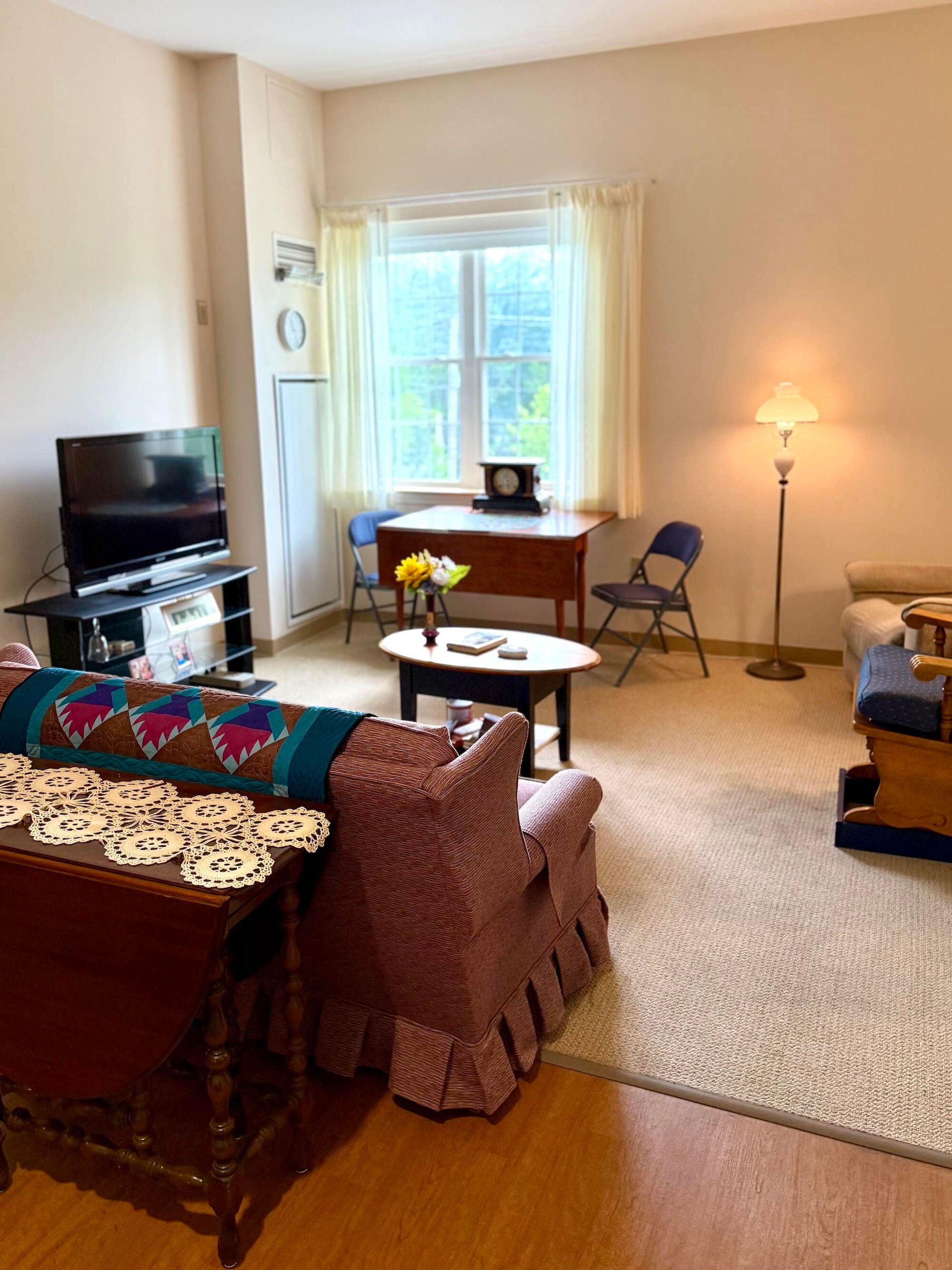 Living room with floral armchair, television, coffee table, and window with natural light.