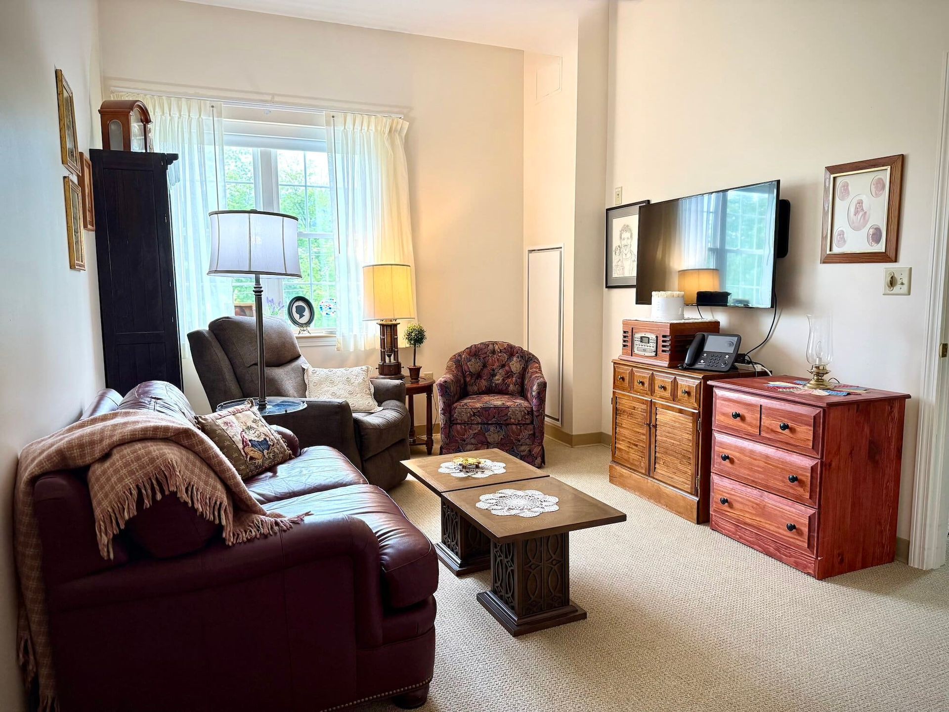Cozy living room with burgundy sofa, floral chair, and wooden furniture; TV on wall.