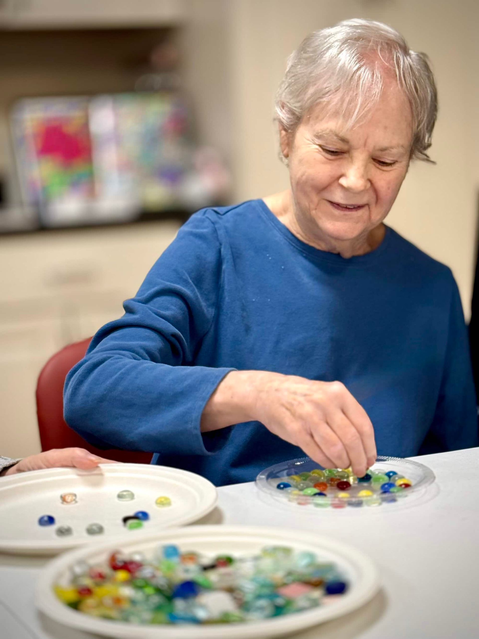 Woman in blue shirt arranging colorful glass gems on a table.