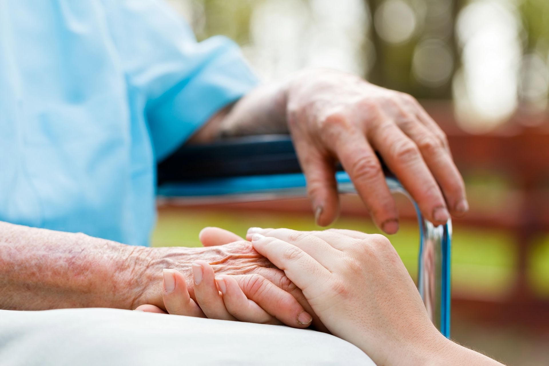Hands of elderly person clasped by younger person, seated outdoors.