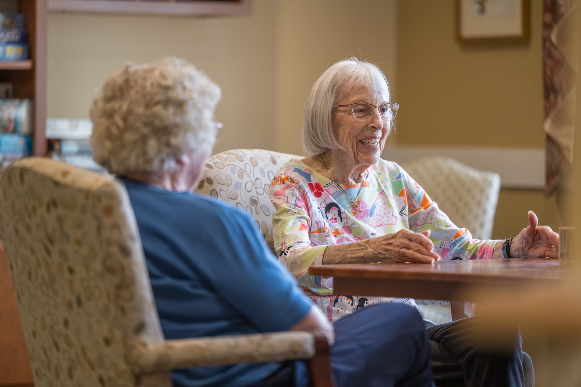 Two people holding hands walking on a path in front of a white house with a yellow roof.