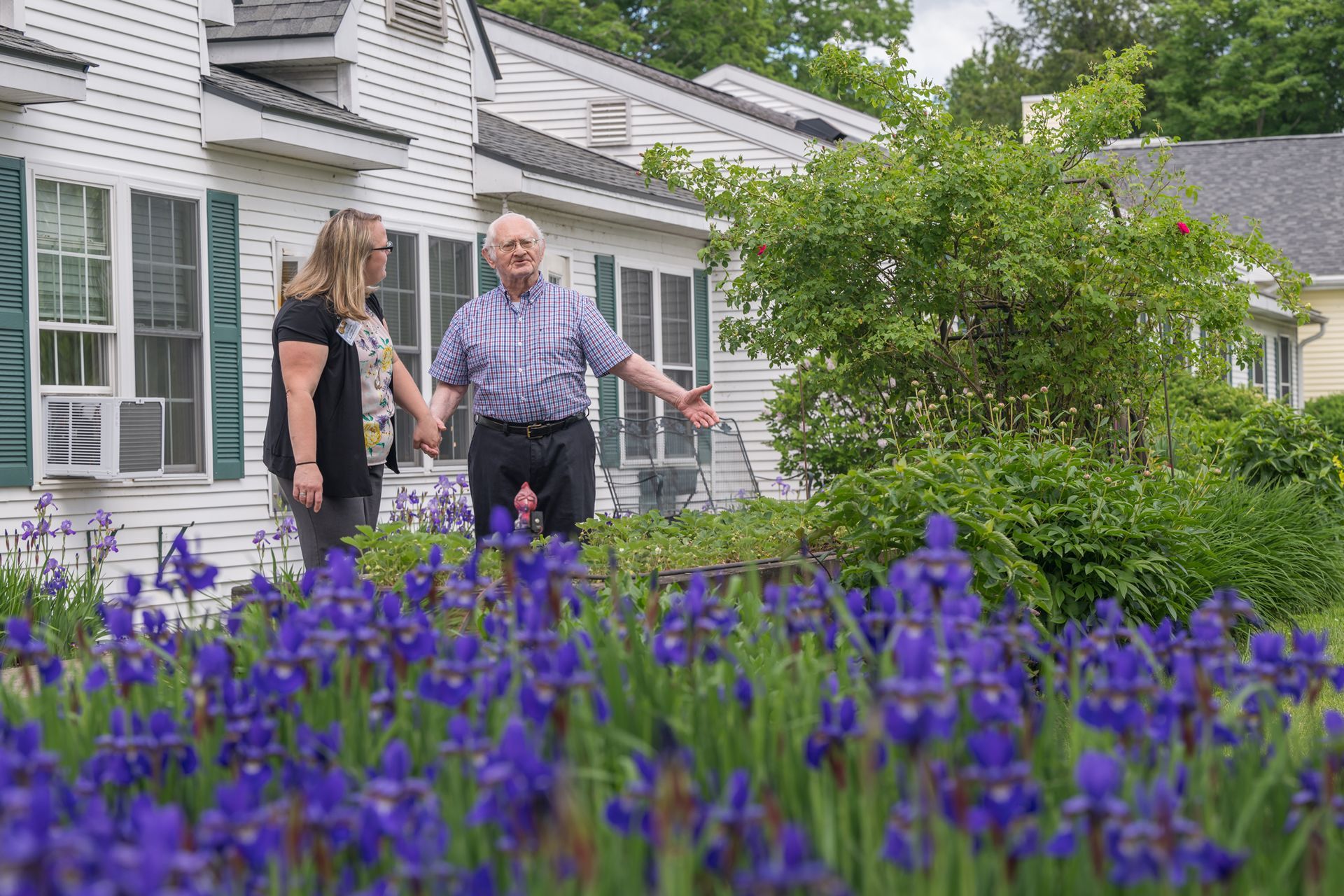 A man and a woman are standing in a garden with purple flowers.