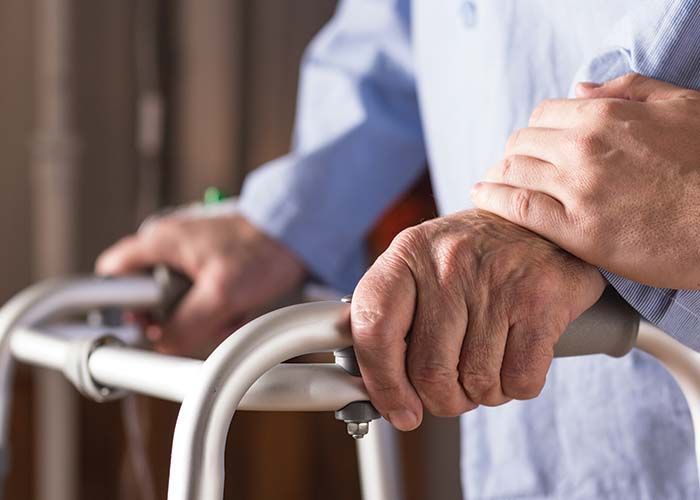 Person using a walker, another hand supporting them.