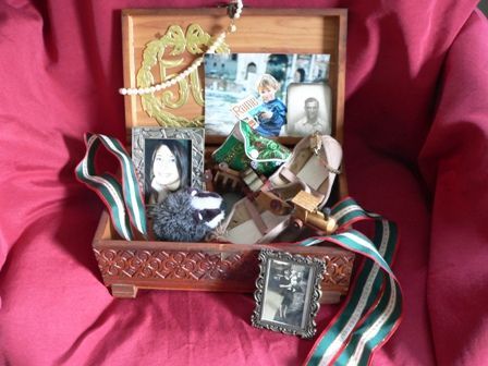 Wooden box with vintage items: photos, ribbons, and shoes on red fabric.