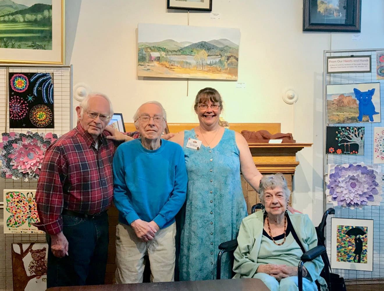 Four people pose in an art gallery, surrounded by paintings. One is in a wheelchair.
