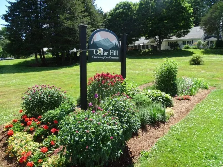 Cedar Hill community sign with flower bed. Green grass, trees, and a house in the background.