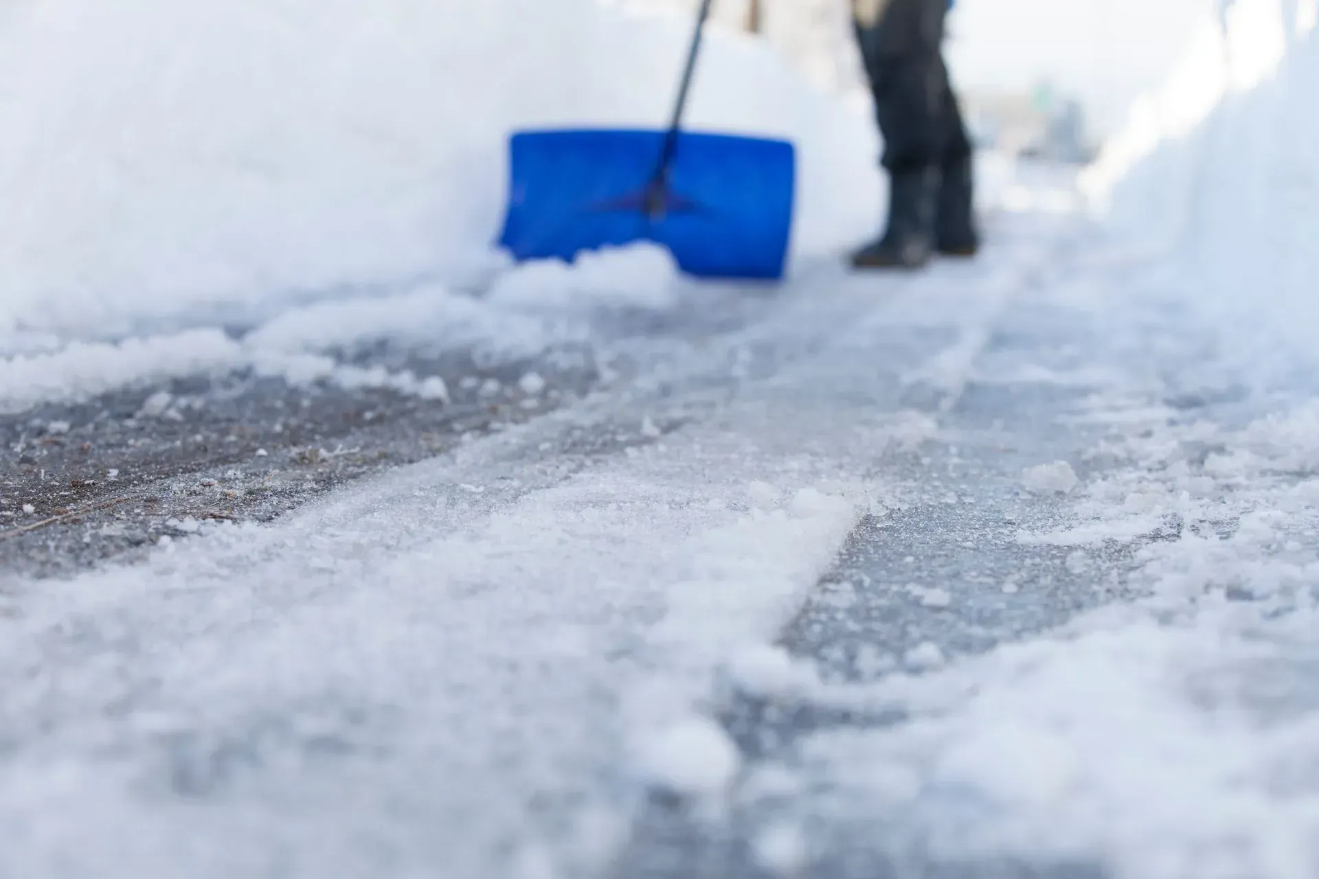 Person shoveling snow from a sidewalk, blue shovel, snowy path, winter.