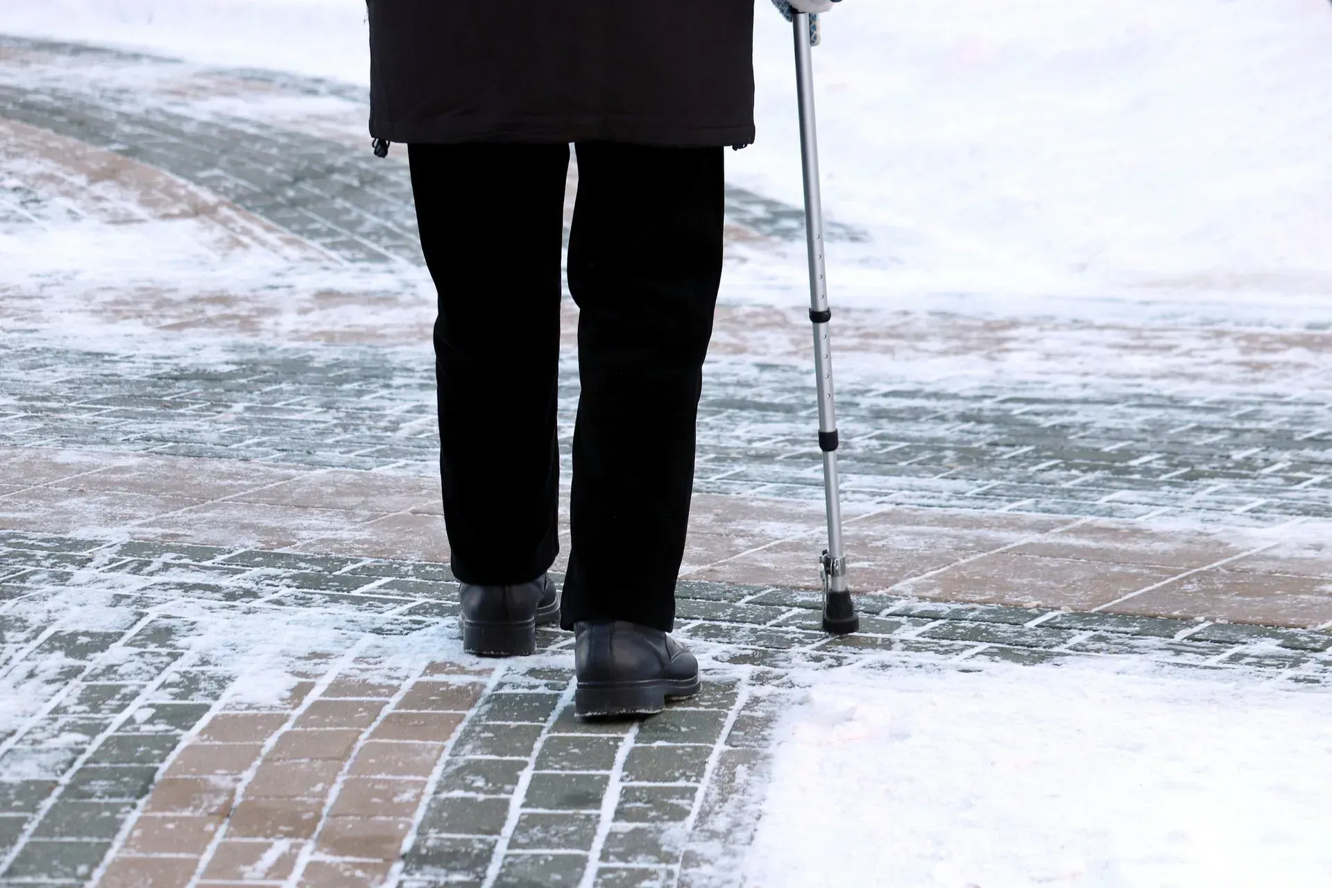 Person walking on a snow-covered brick path, using a cane for support.
