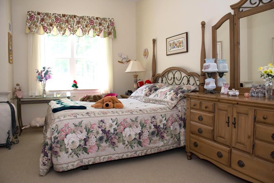 Bedroom with floral bedding, wooden furniture, a window, and a stuffed bear.