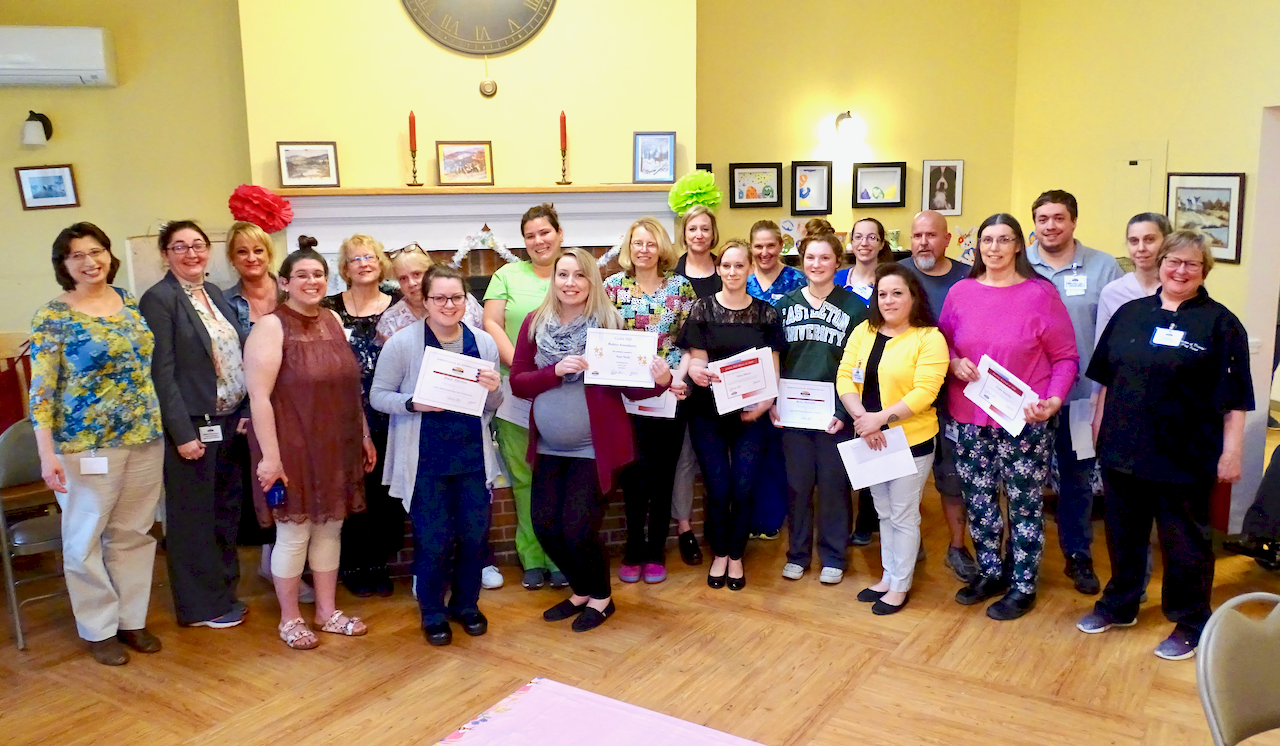 Group of people holding certificates, posing in a room with framed art on the walls.