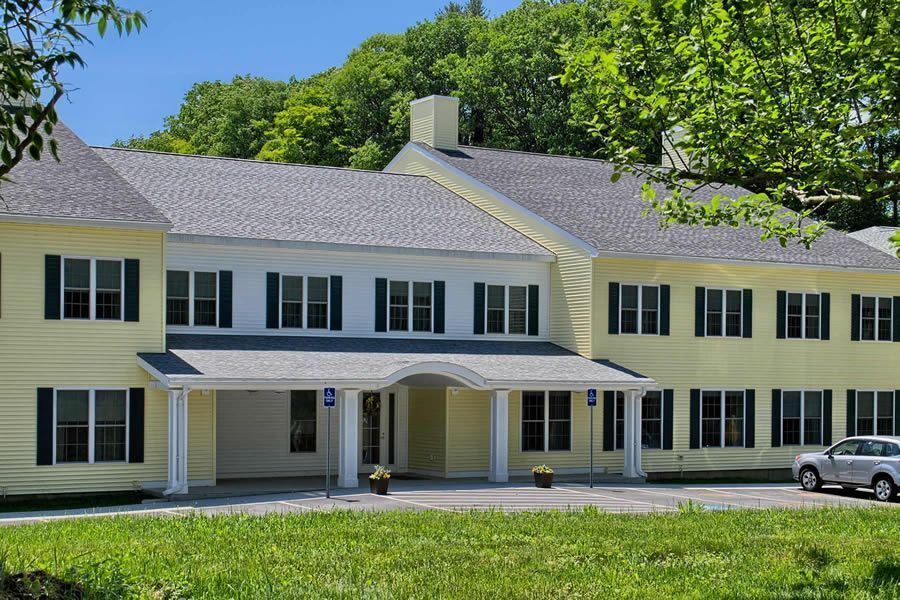 Two-story yellow building with dark shutters and gray roof. Front entrance under a covered porch.