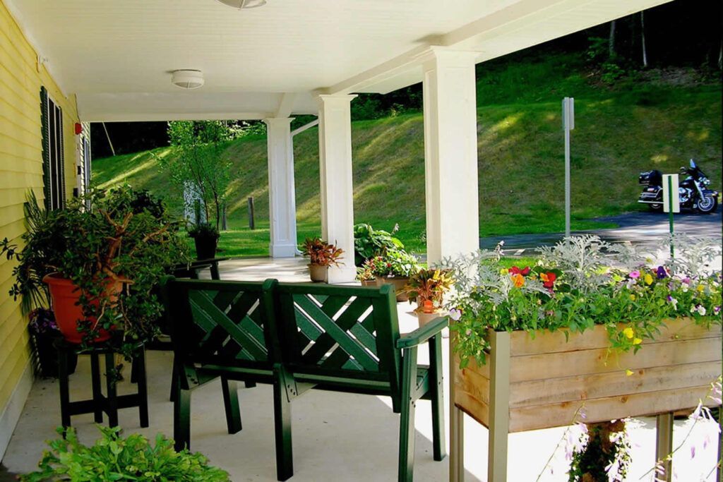 Covered porch with green bench and planters; hillside in the background.