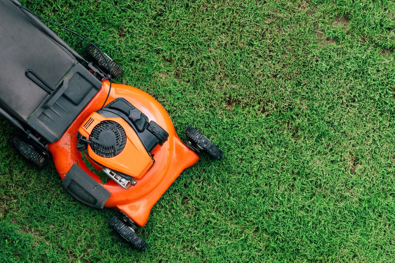 Orange lawnmower on green grass, top-down view. Orange lawnmower on green grass, top-down view.