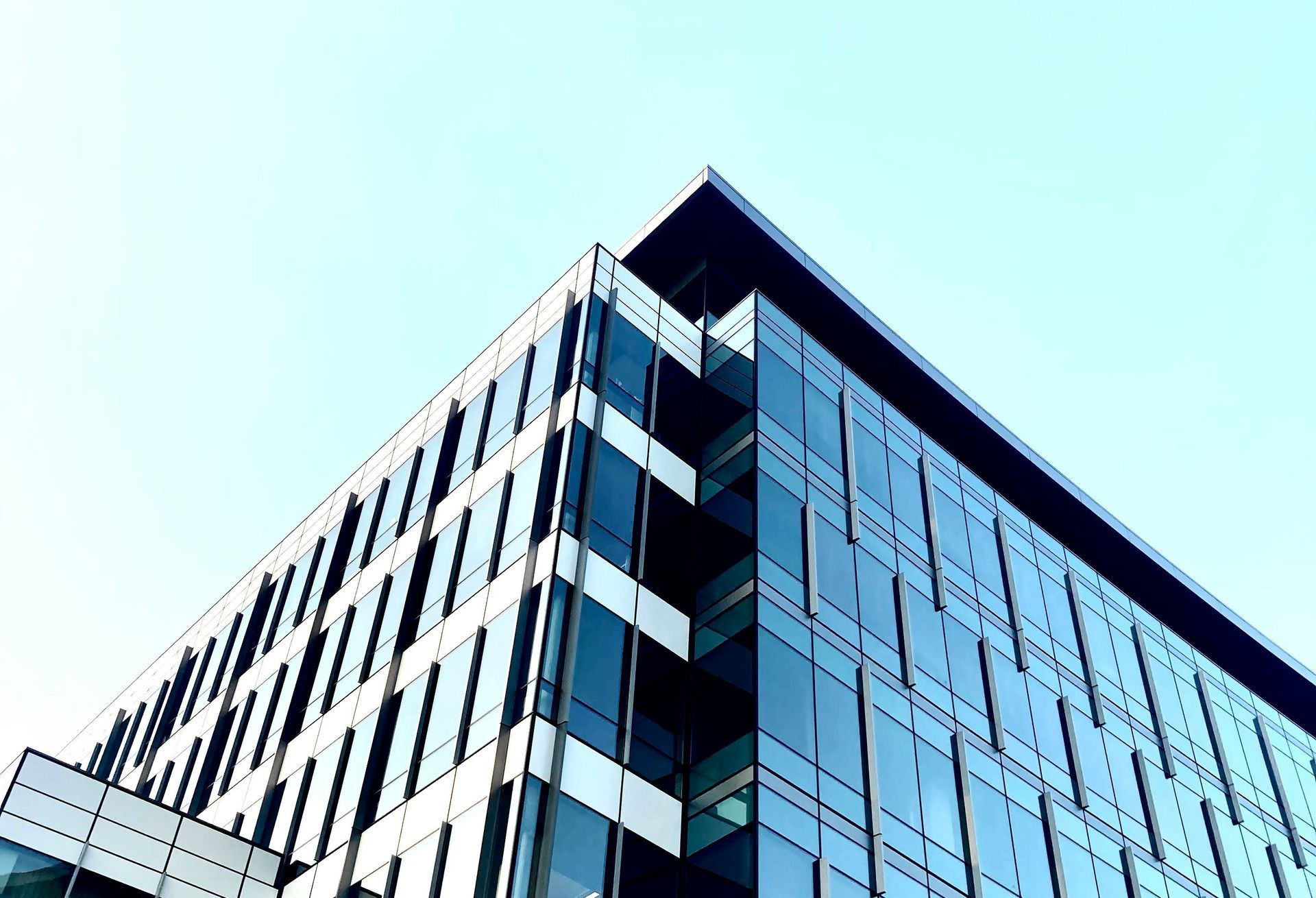 Modern office building with glass facade, angled view against a light blue sky.
