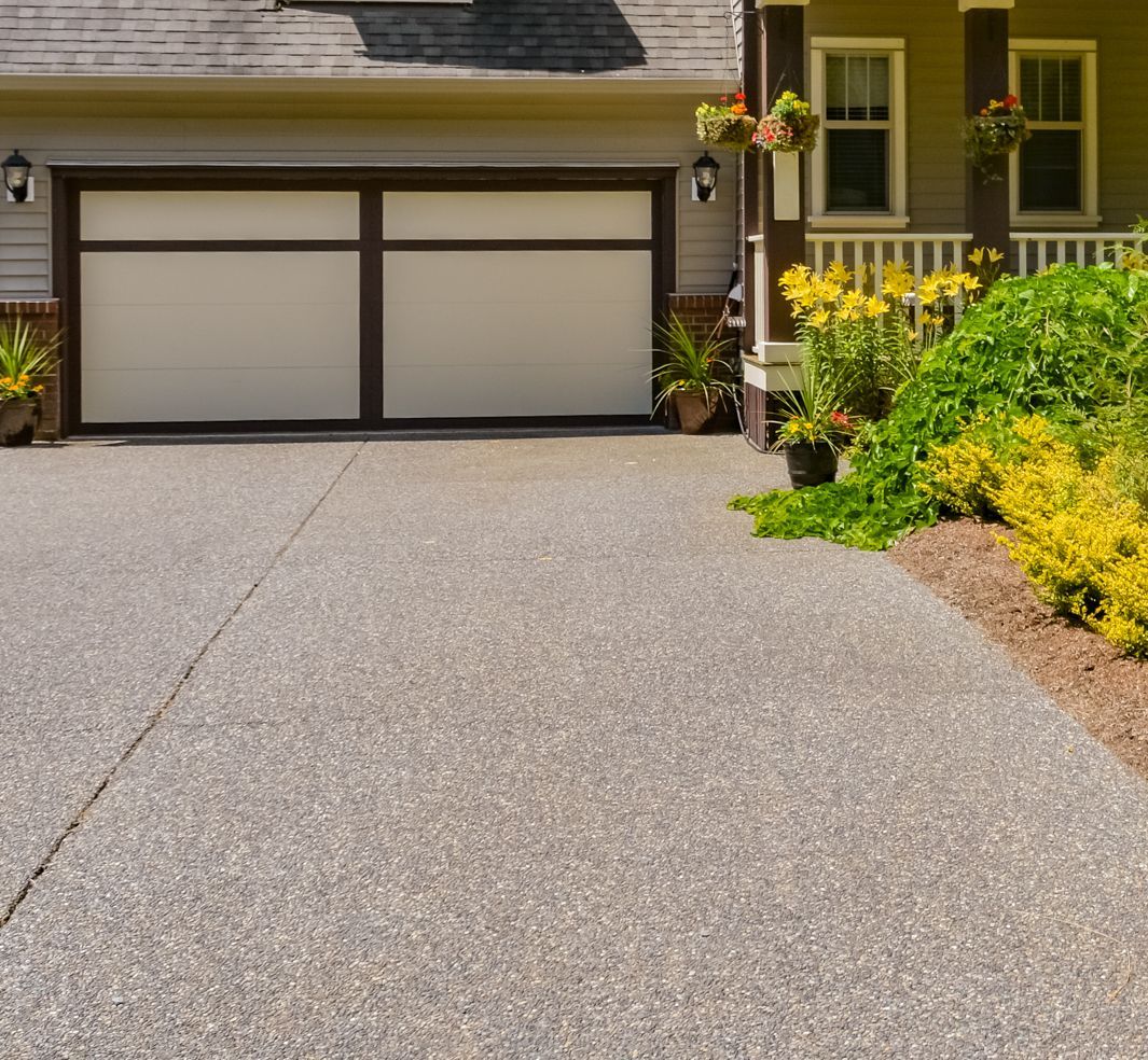 Concrete driveway leading to a house with a beige garage door and lush landscaping.