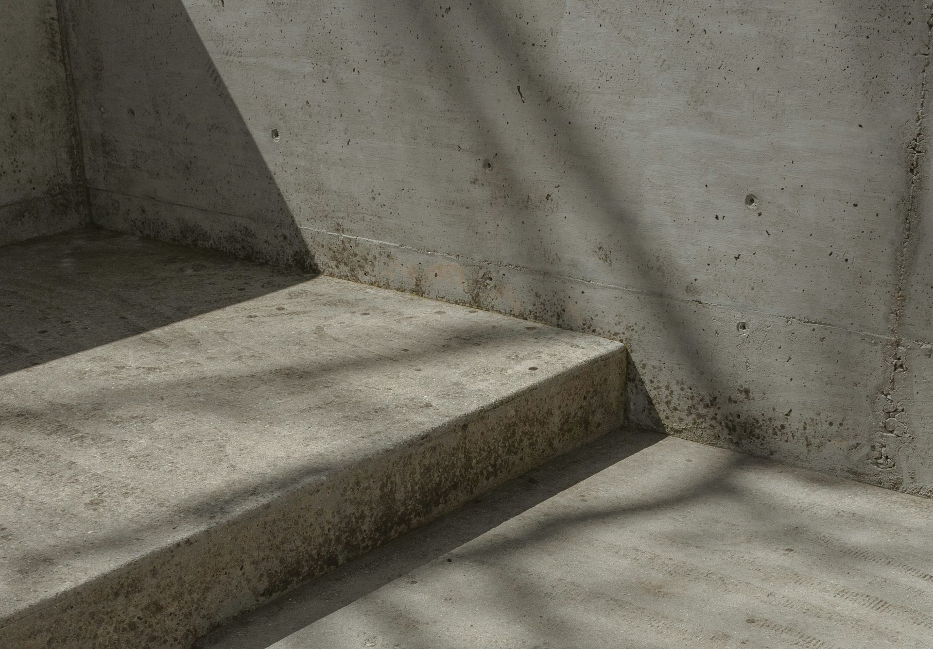 Concrete corner with a step. Harsh sunlight casts shadows on the rough surface.
