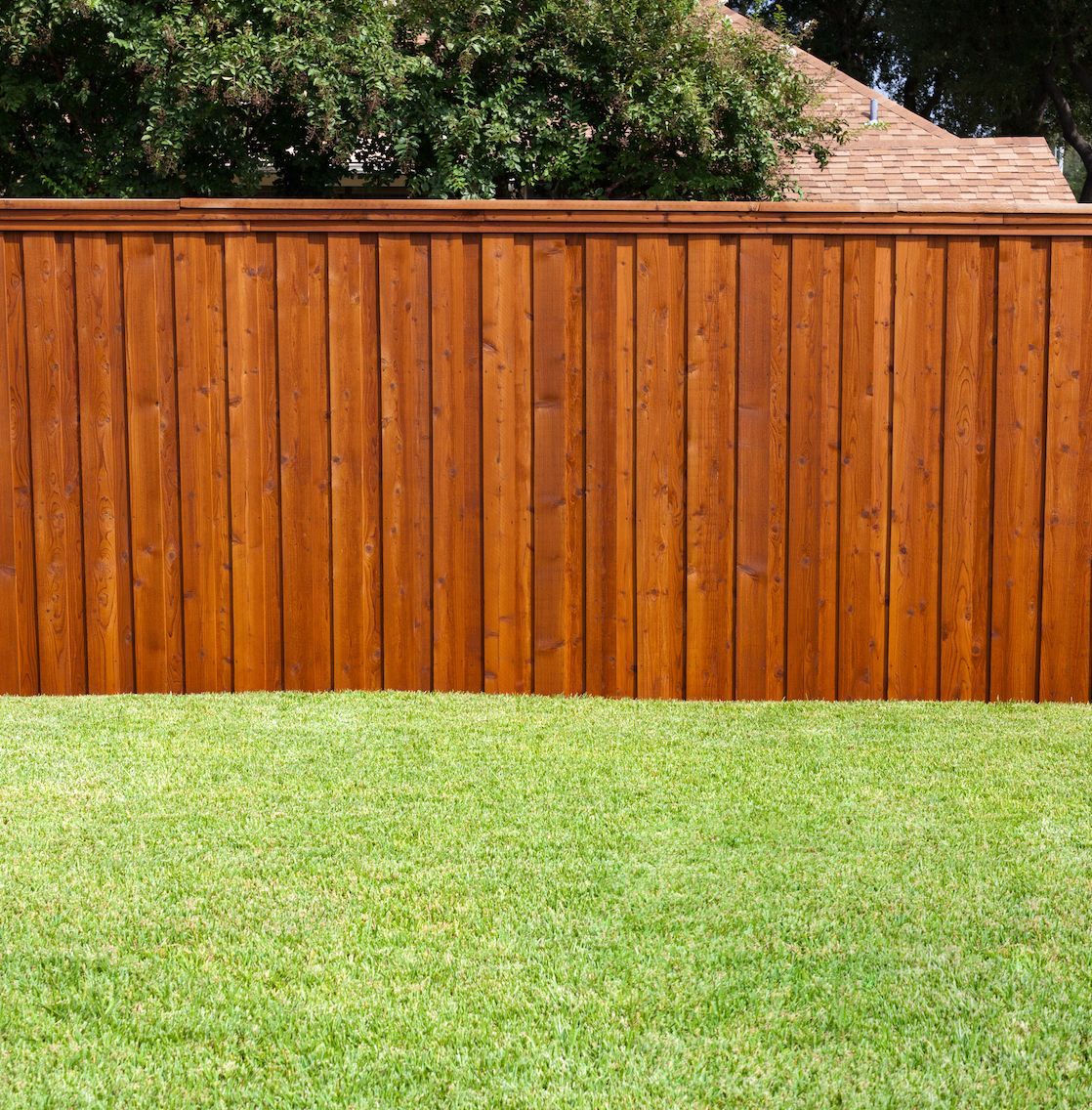 Wooden fence stained brown against a green grassy lawn.