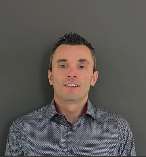 Person in a patterned shirt posing against a plain gray background.