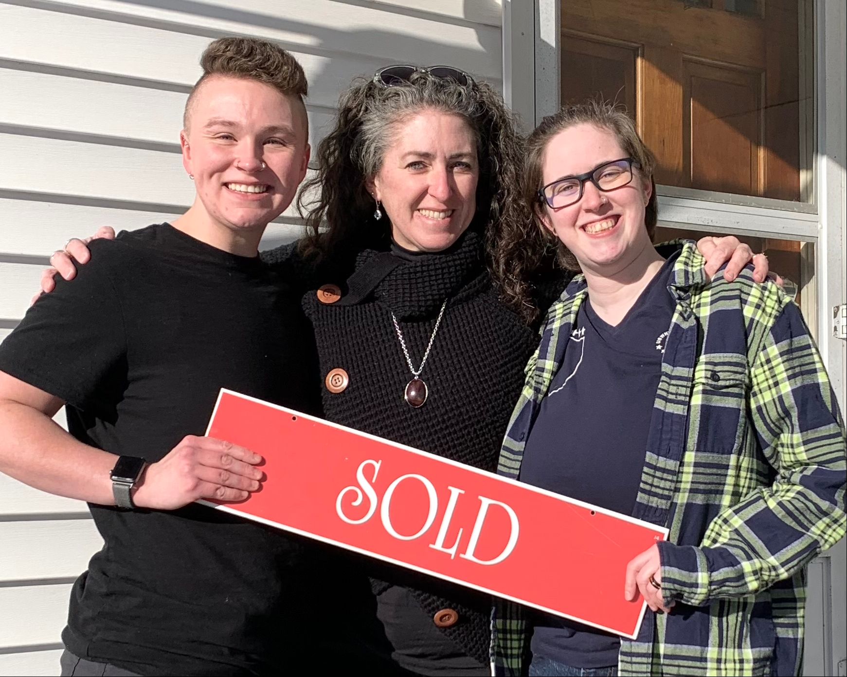 Three people are holding a sold sign in front of a house.