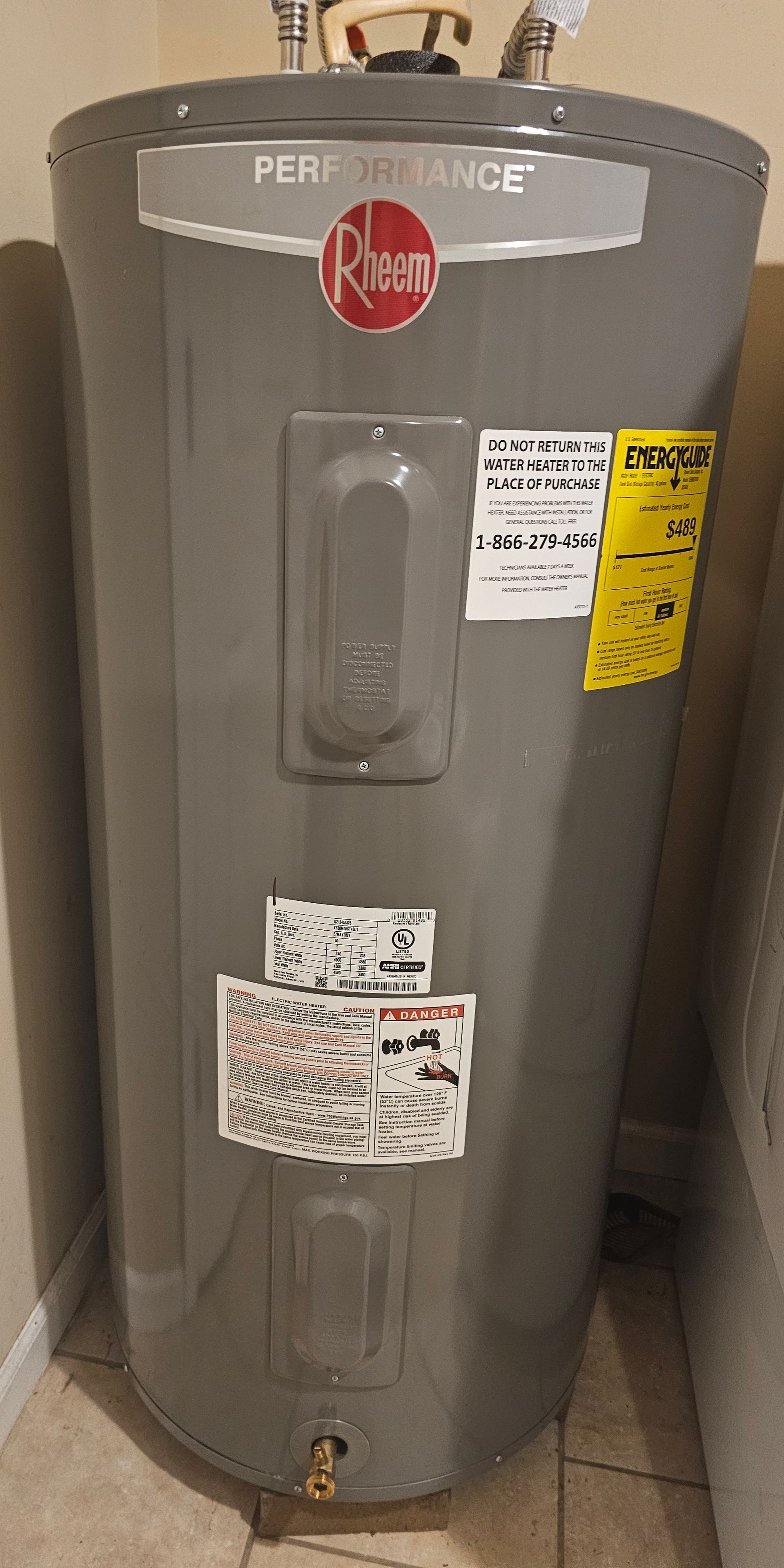 A gray water heater is sitting on a tiled floor next to a wall.