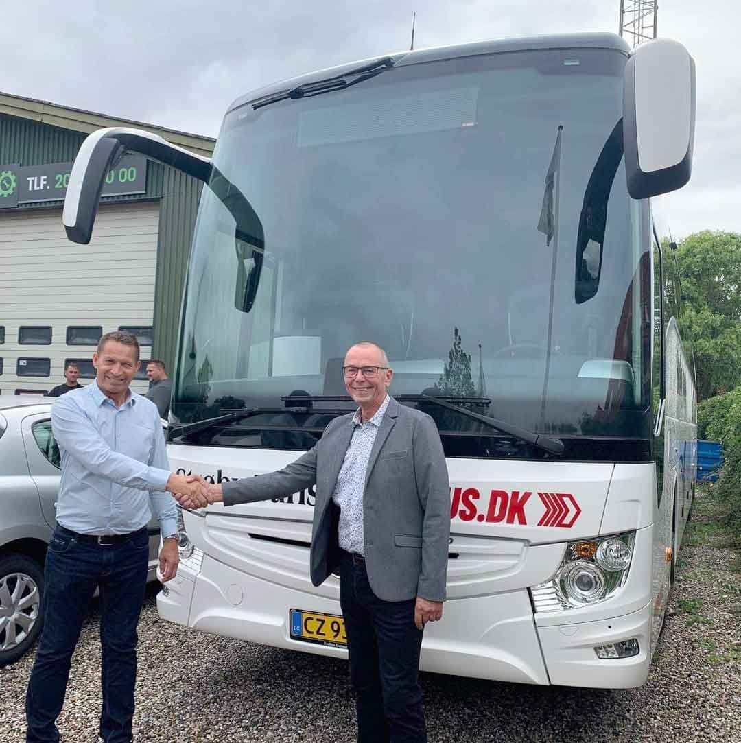 To mænd giver hånd foran en hvid turistbus med .DK på.