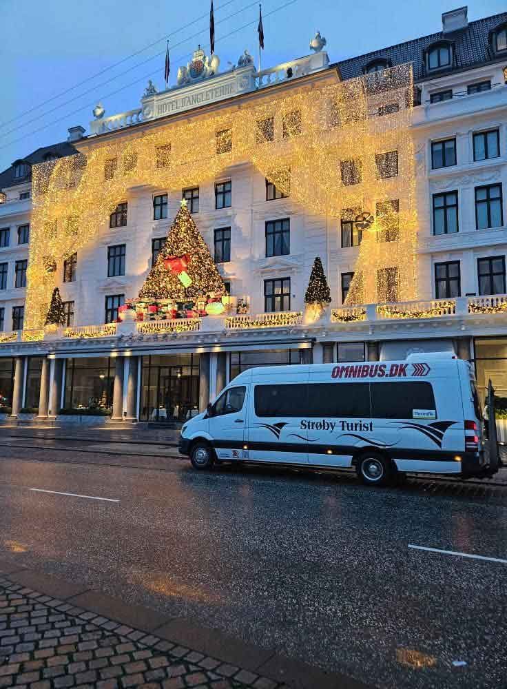 Hvid varevogn foran en bygning dekoreret med julelys; København, Danmark.