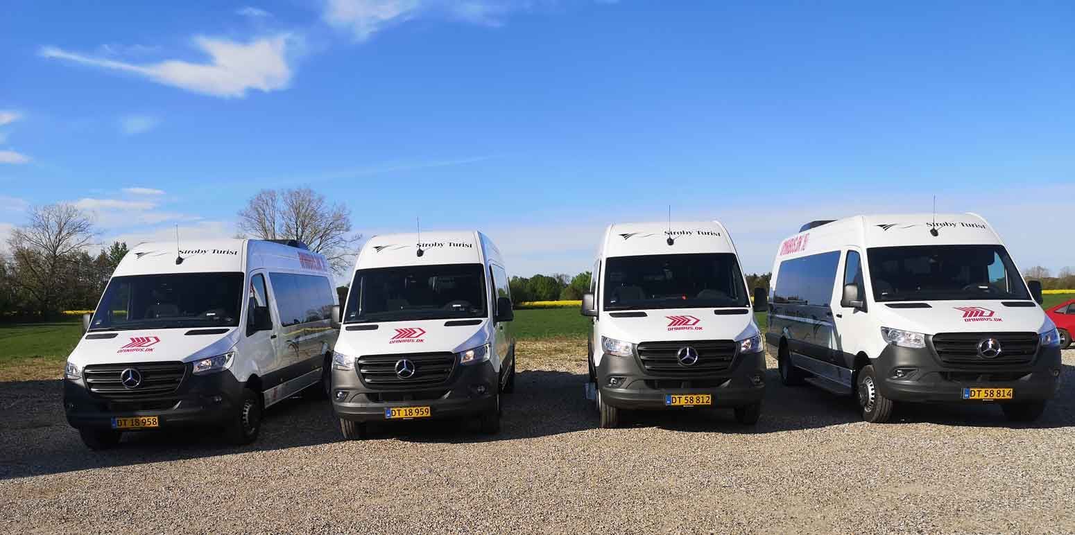 Fire hvide varevogne med røde logoer parkeret på grus under en blå himmel.